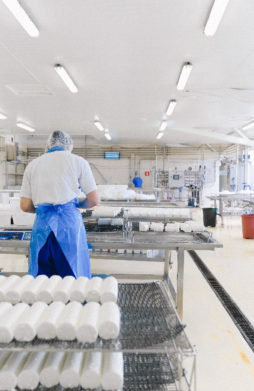 Workers in hairnets and frocks seen from behind at a processing line, with product moving past them on the belt.